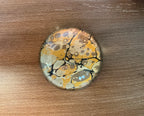 A domed glass paperweight on a wooden table, over hand marbled paper in ochre and black with a crackled pattern.
