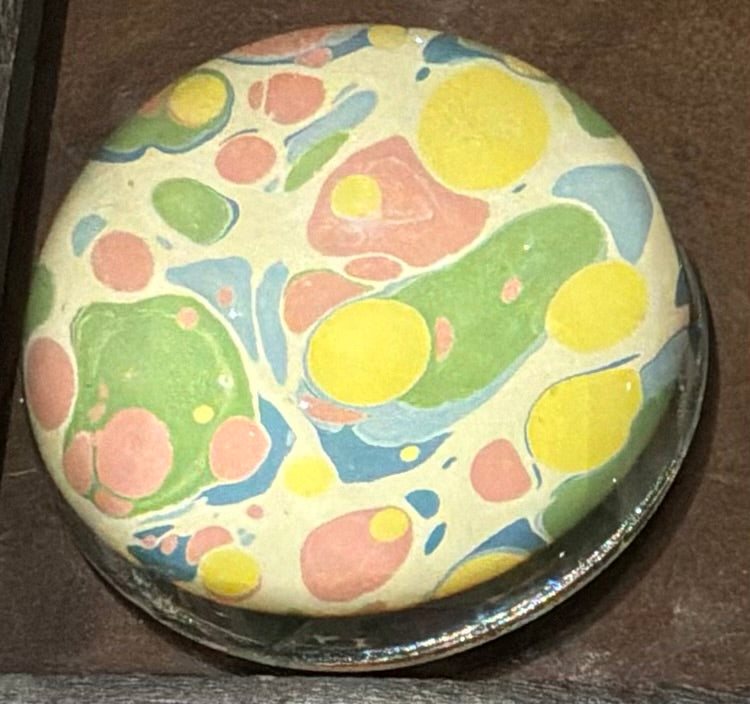 Compton Marbling Glass Paperweight on a Cream Background with Sunny Yellows, Coral Pink and shades of Blue and Green.