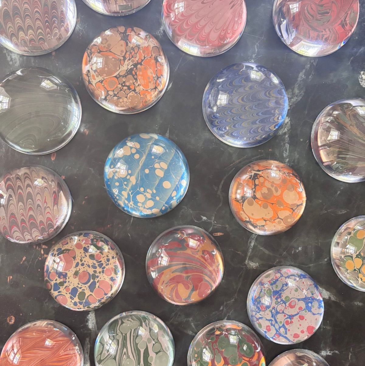 Compton Marbling Glass Paperweight on a Cream Background with Sunny Yellows, Coral Pink and shades of Blue and Green.