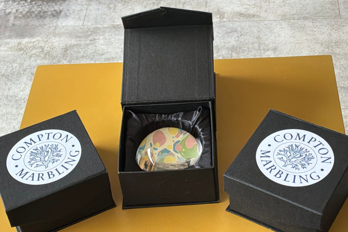 Compton Marbling Glass Paperweight on a Cream Background with Sunny Yellows, Coral Pink and shades of Blue and Green.